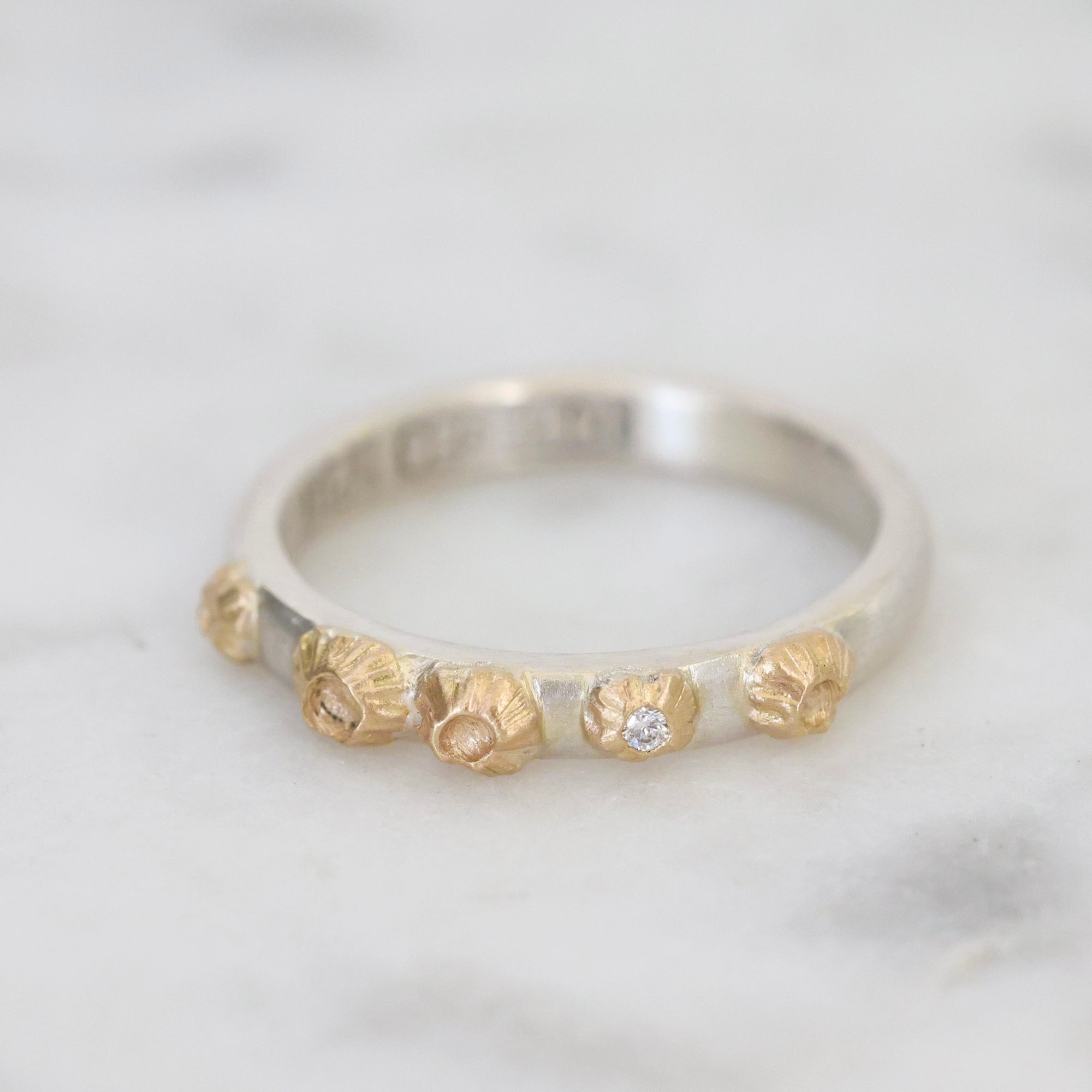 Silver ring with gold accents and a diamond on a light gray background