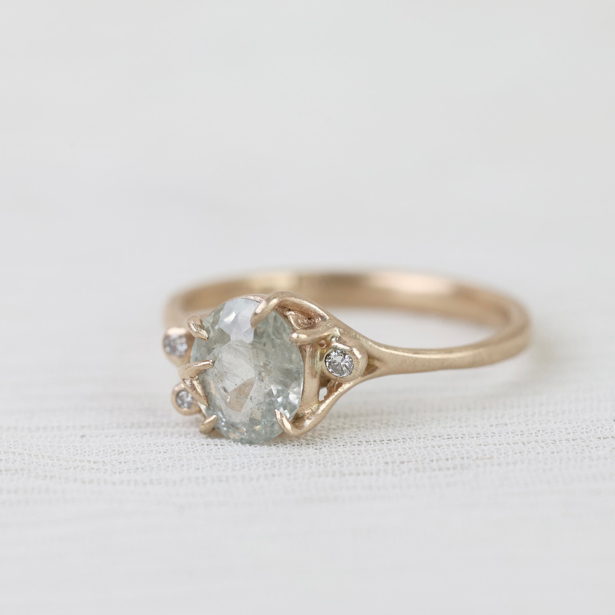 Gold ring with a pear-shaped white sapphire on a light fabric background