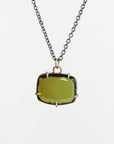 A necklace featuring a large, cushion-cut olive green gemstone in a gold bezel setting, suspended from a dark gunmetal chain against a light gray background.