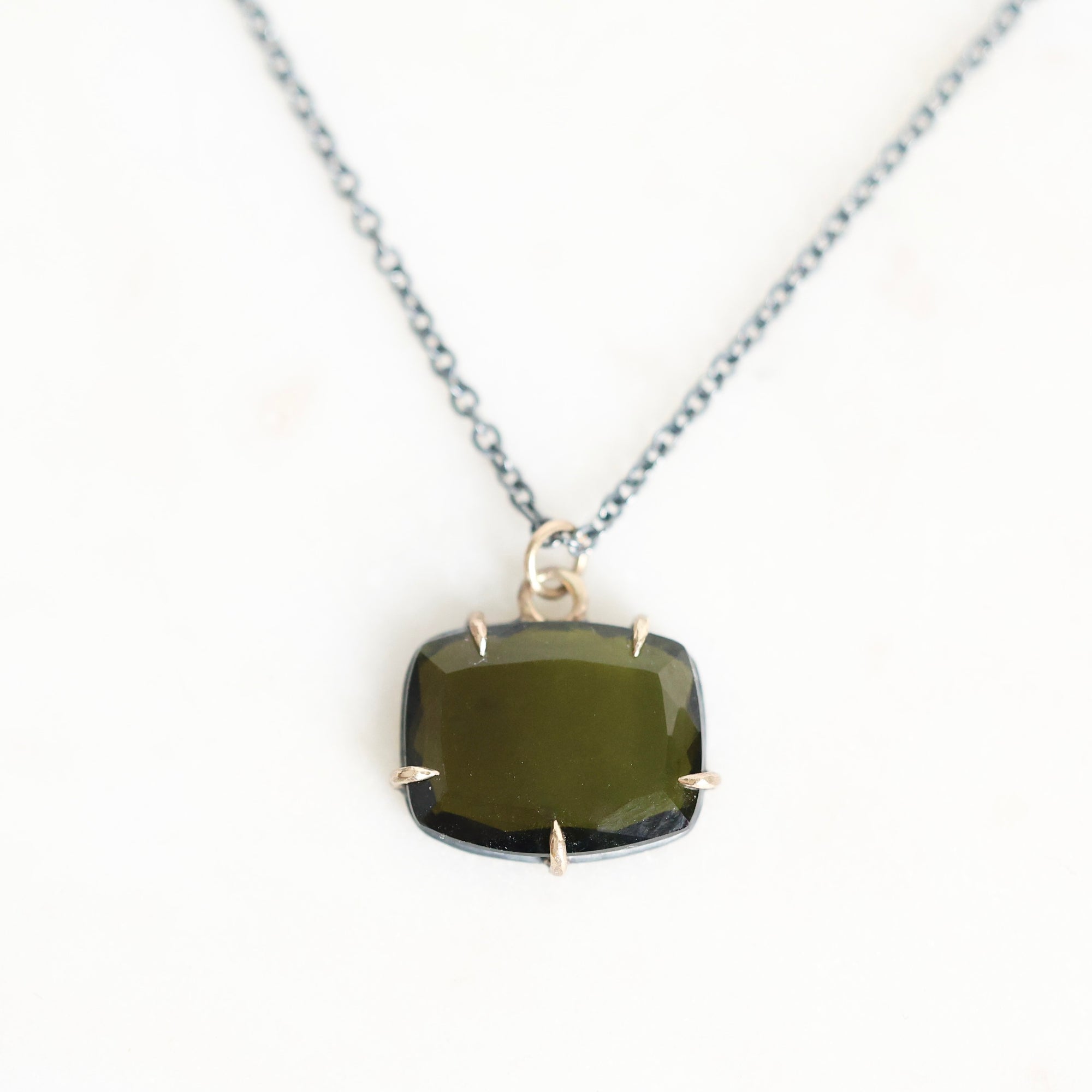 A silver chain necklace with a cushion-cut dark green gemstone pendant in a prong setting, displayed on a clean white background.
