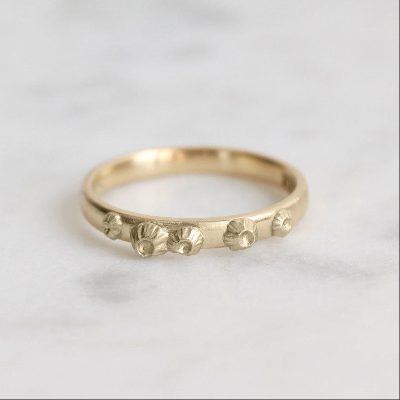 Gold ring with barnacle designs on a light gray background