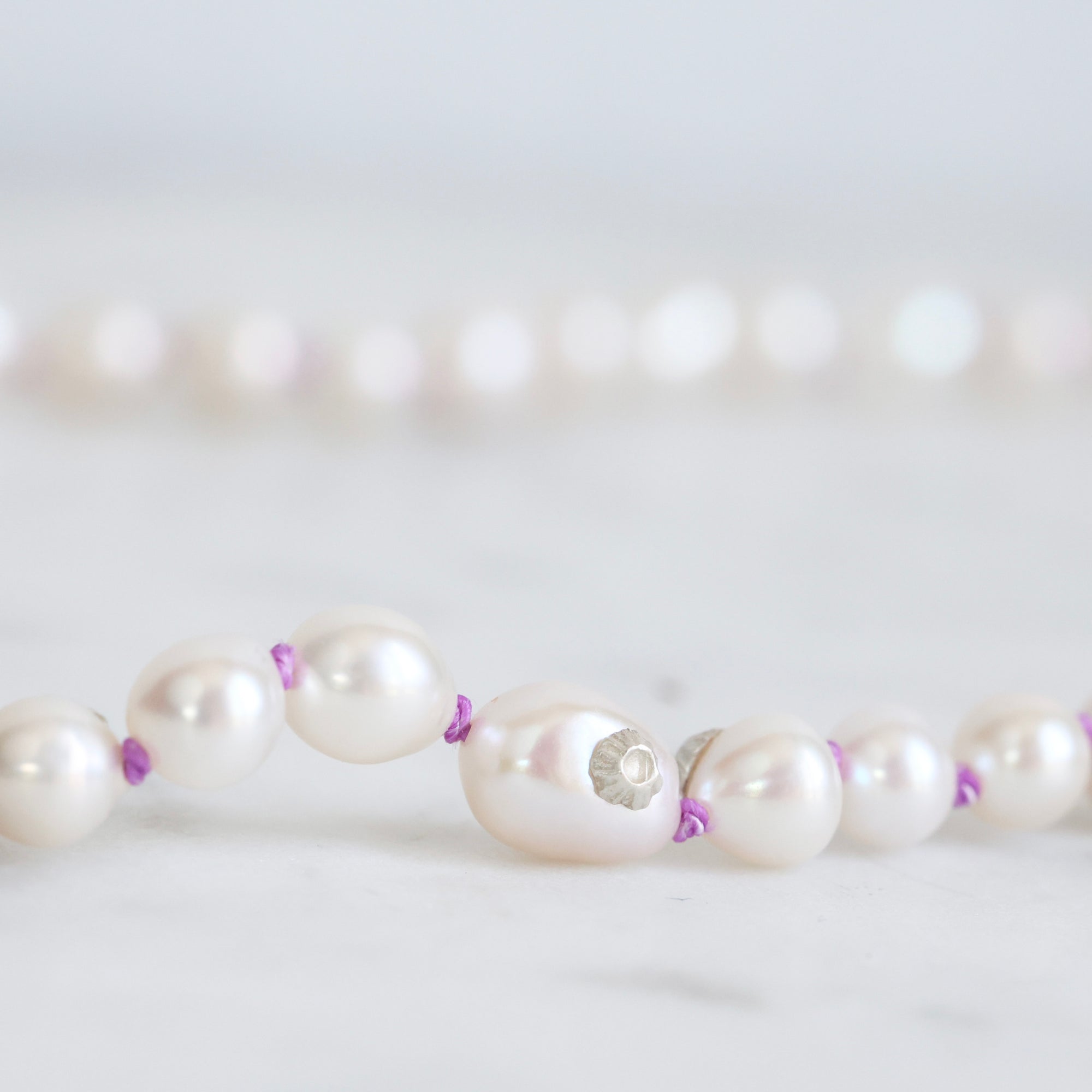 Pearl necklace with purple accents on a light gray background