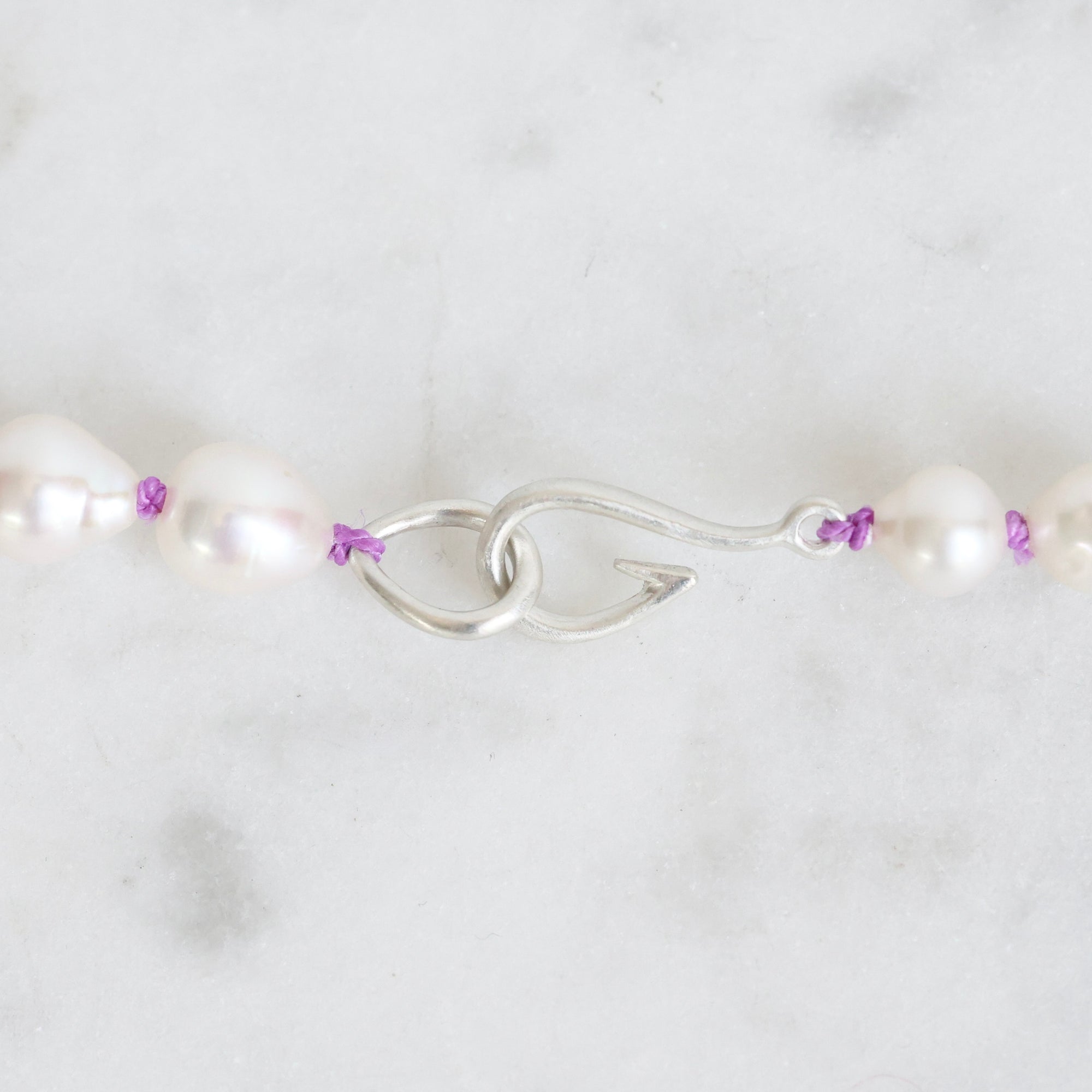 Pearl necklace with silver clasp and purple beads on a white background
