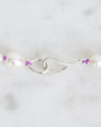Pearl necklace with silver clasp and purple beads on a white background