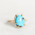 A gold ring featuring an oval turquoise cabochon with natural brown matrix inclusions, set in a prong-style gold band against a clean white background.