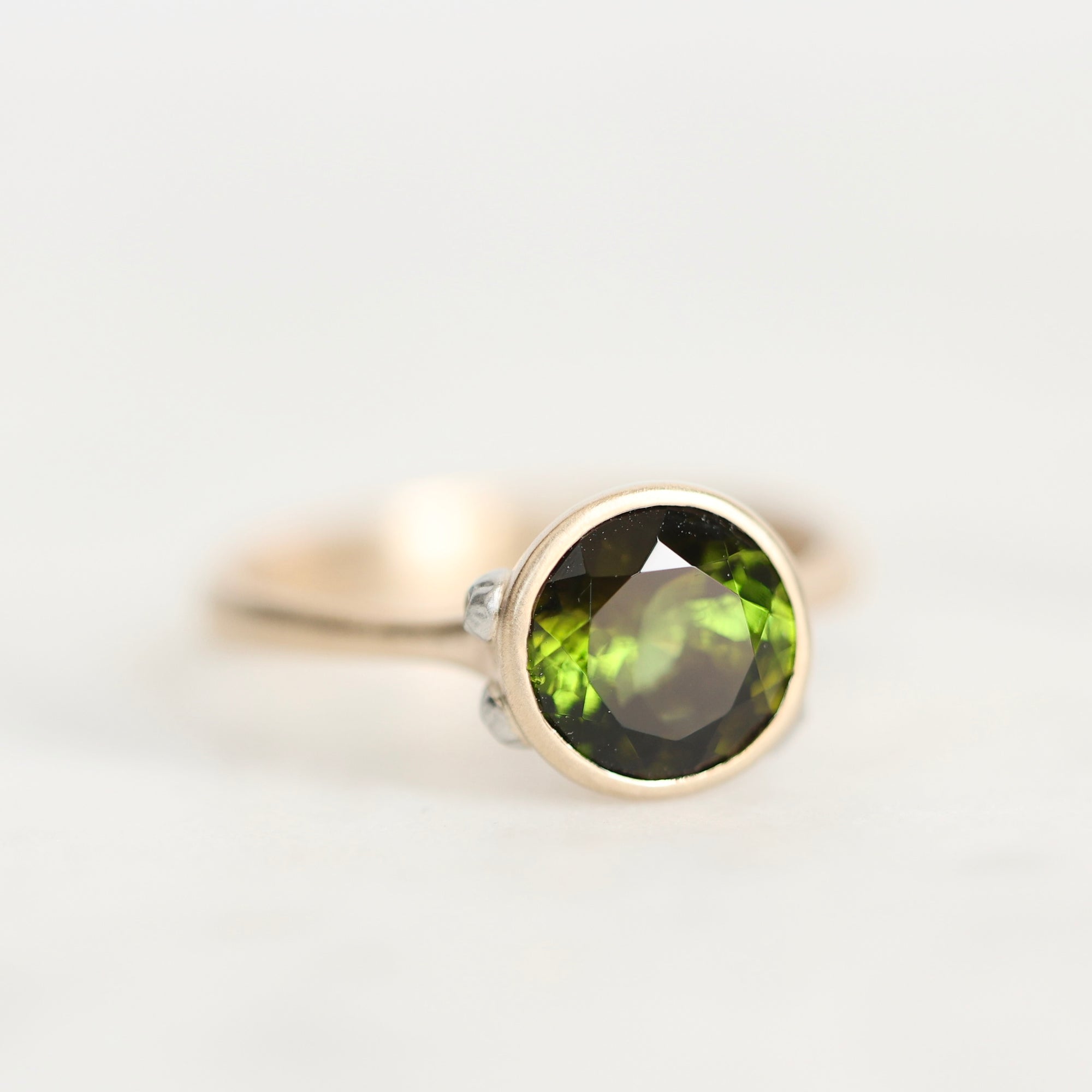 A round-cut green gemstone ring set in a gold-toned bezel with a silver-toned band, photographed on a clean white background.
