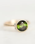 A round-cut green gemstone ring set in a gold-toned bezel with a silver-toned band, photographed on a clean white background.