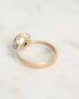 A gold ring with a sculpted dome-shaped top set with small clear stones and a tiny green accent, resting on a light marble surface.