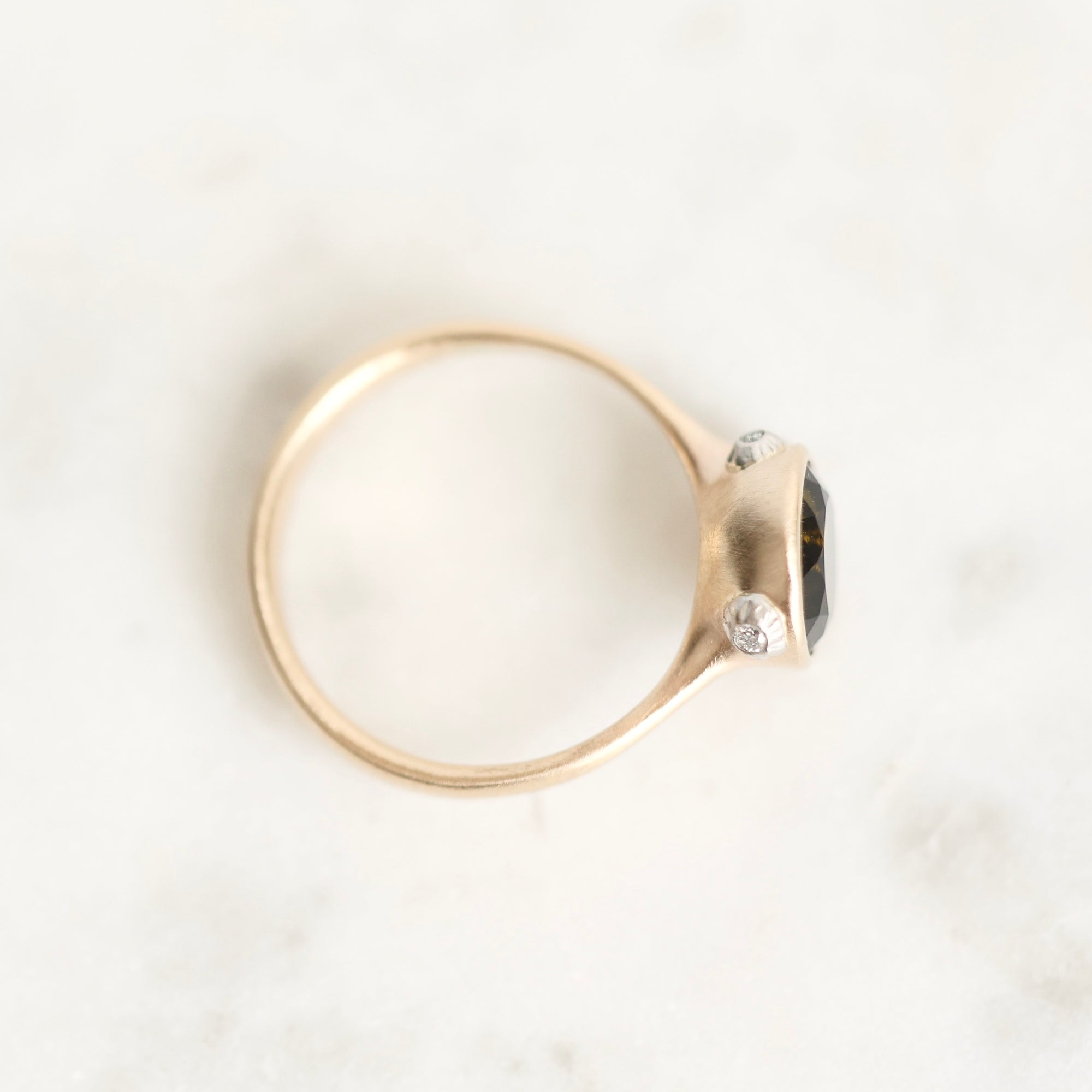 A gold ring with a dark gemstone and two small clear accent stones, photographed on a light marble-like surface.