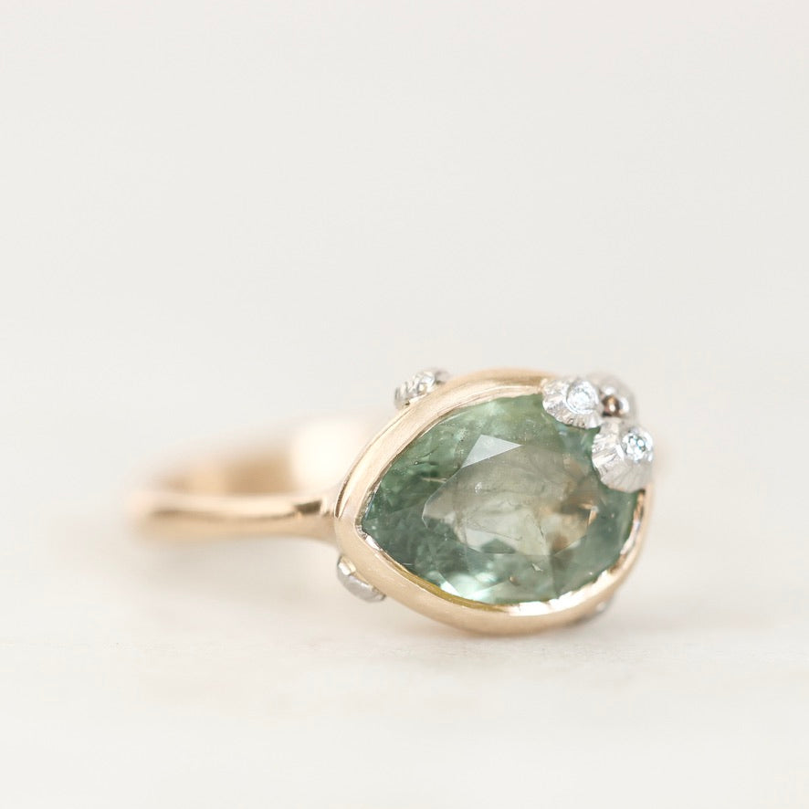 A pear-shaped green gemstone ring in a gold setting with small clear accent stones, photographed on a clean white background.