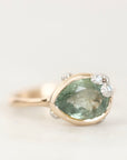 A pear-shaped green gemstone ring in a gold setting with small clear accent stones, photographed on a clean white background.