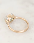 A close-up shot of a yellow gold ring with a cluster of small clear stones on a light marble surface.