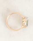 A gold ring with a large green gemstone and small clear accent stones, photographed on a light marble surface.