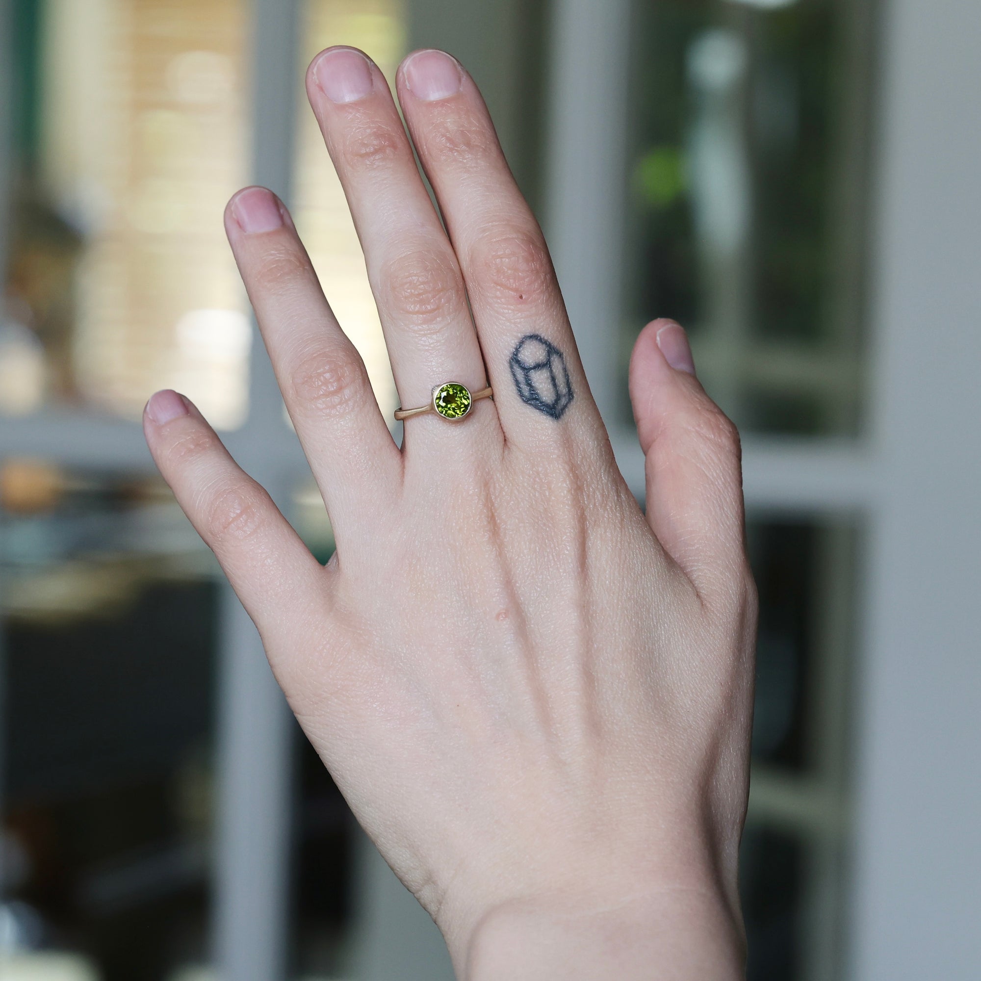 Hand with a green gemstone ring and black tattoo on a blurred background
