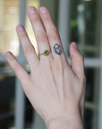 Hand with a green gemstone ring and black tattoo on a blurred background