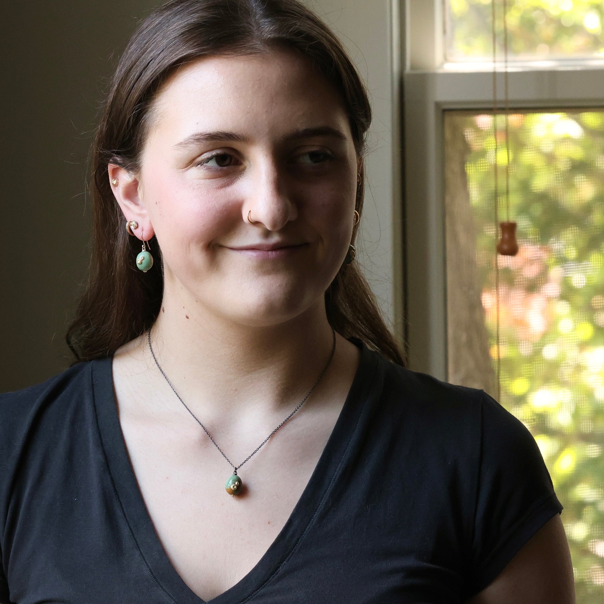 Woman wearing a black top and necklace with a blurred window background