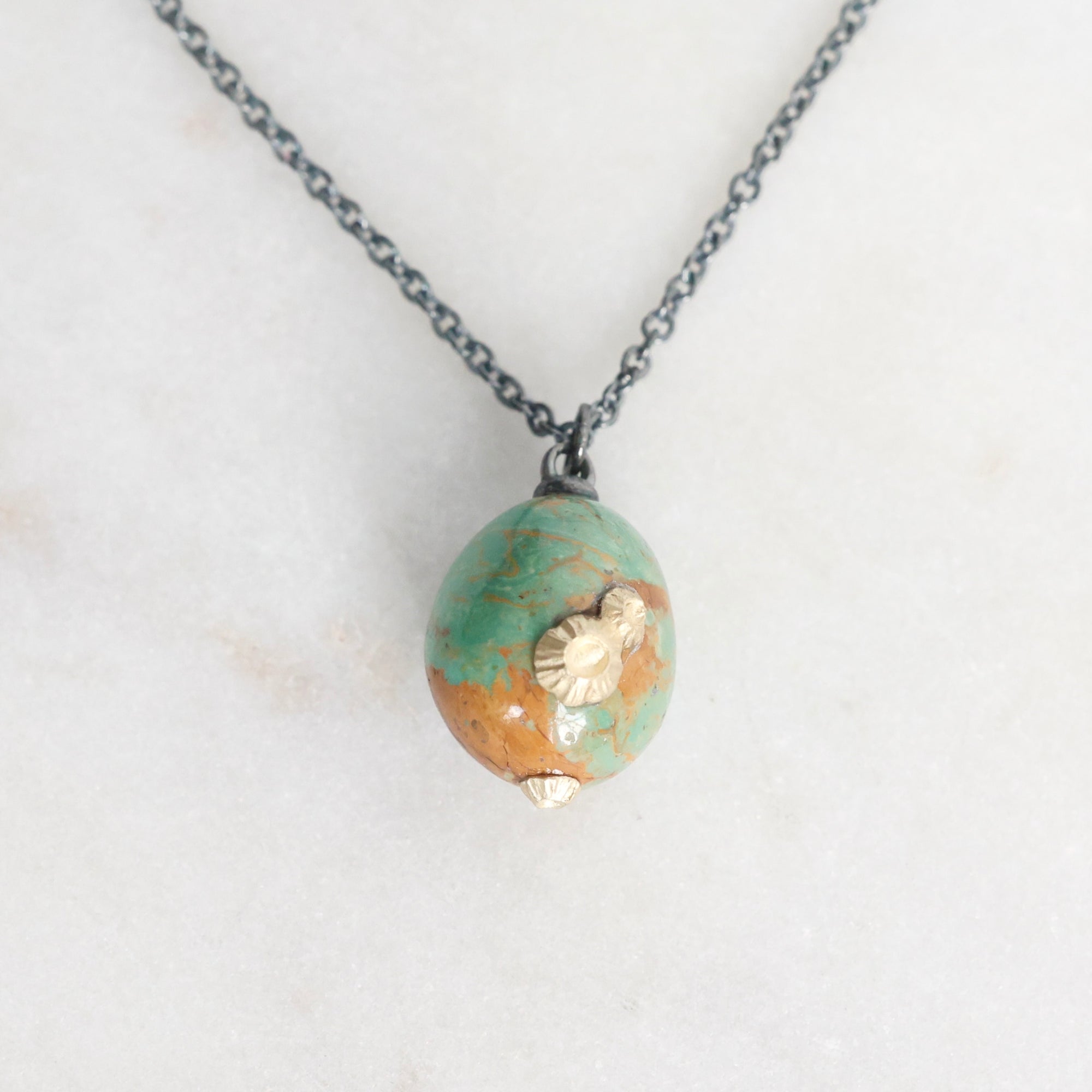 Necklace with a green and gold bead pendant on a light background