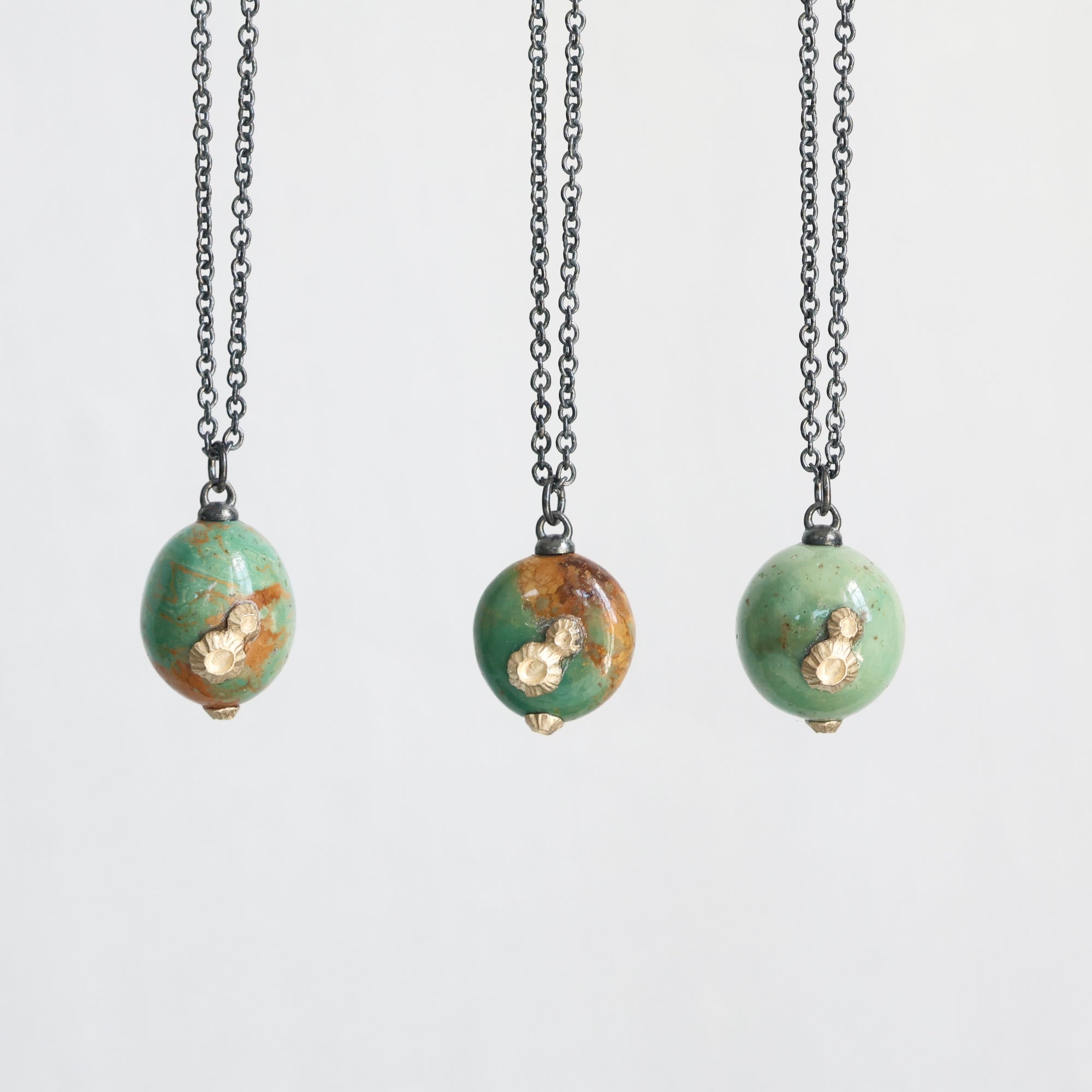 Three necklaces with green bead pendants on a white background