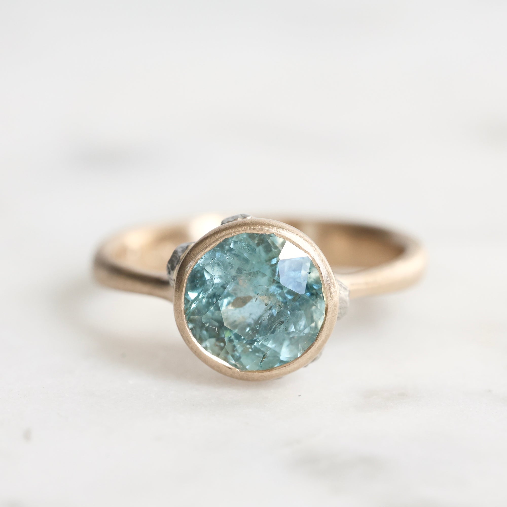 Gold ring with a greenish-blue gemstone on a light background