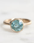 Gold ring with a greenish-blue gemstone on a light background