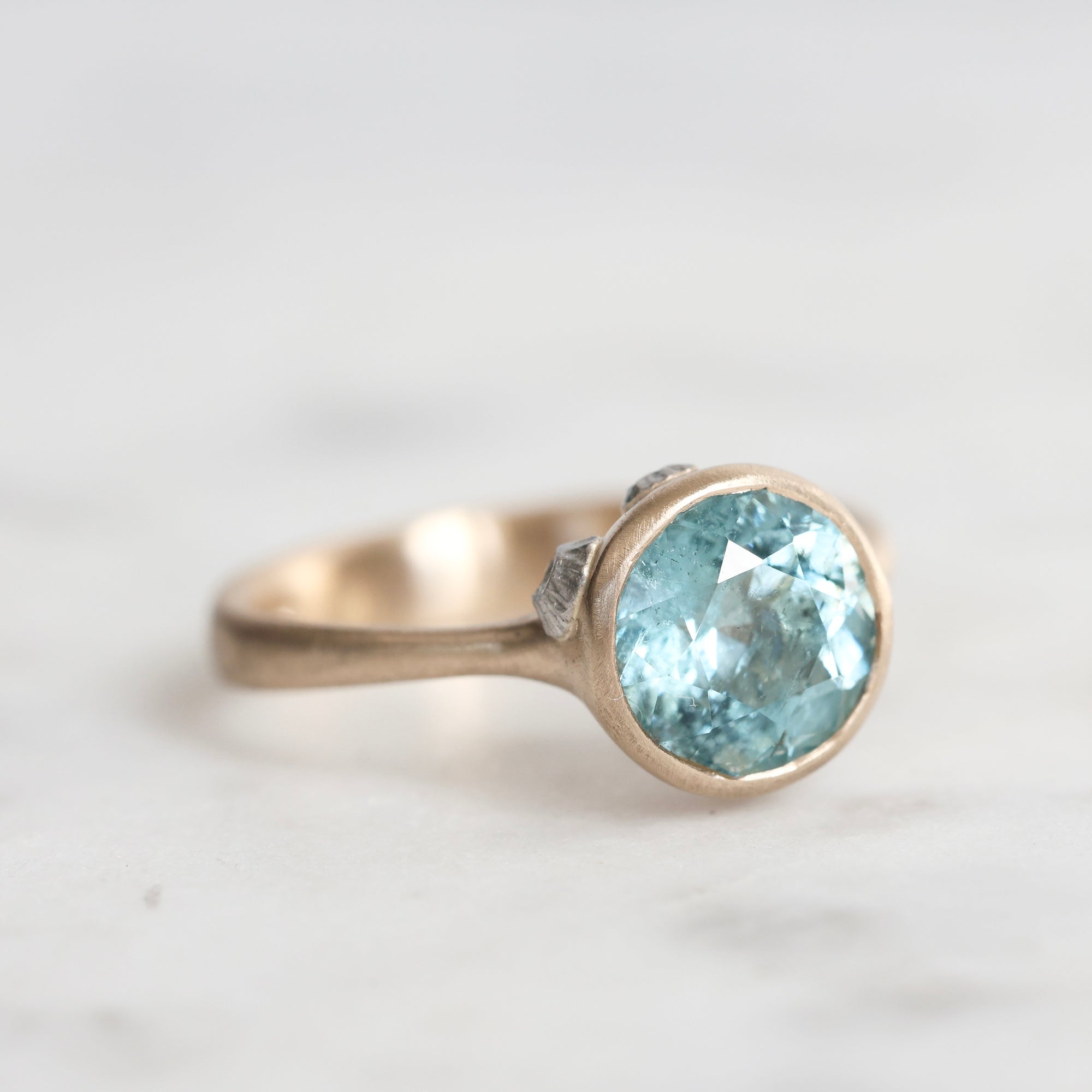 Gold ring with a blue gemstone on a light gray background