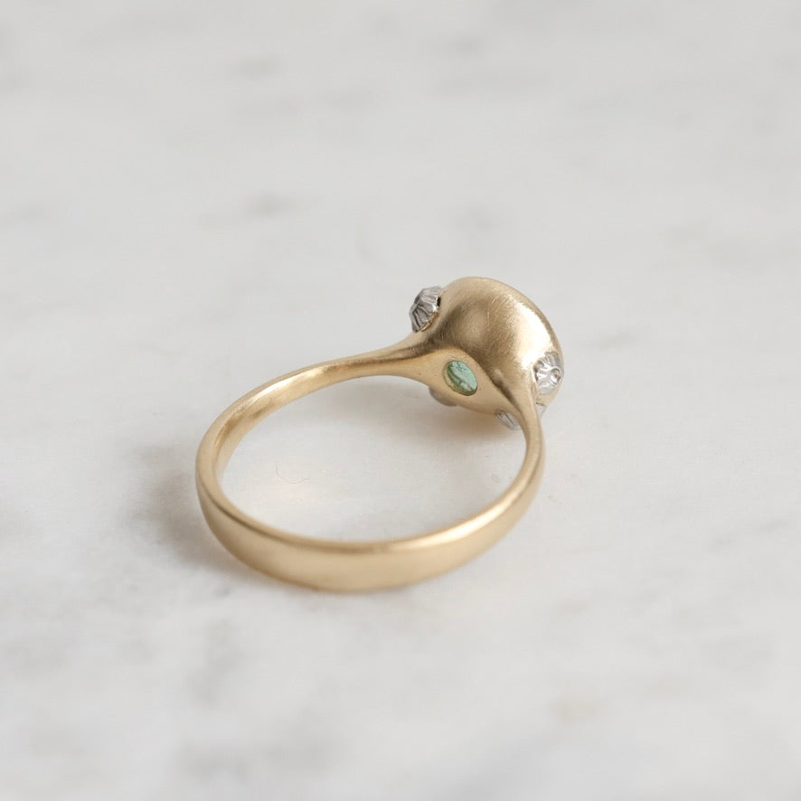 Gold ring with a green gemstone on a light gray background