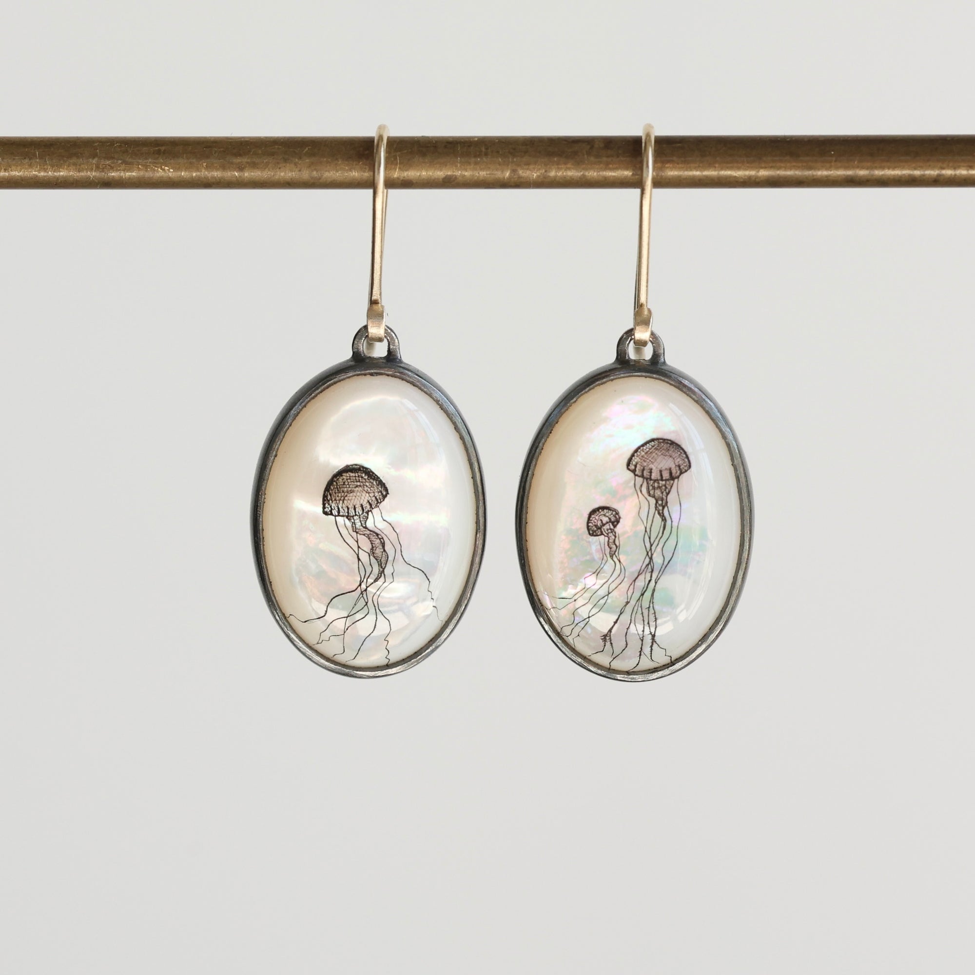 Oval-shaped earrings with jellyfish design on a gray background
