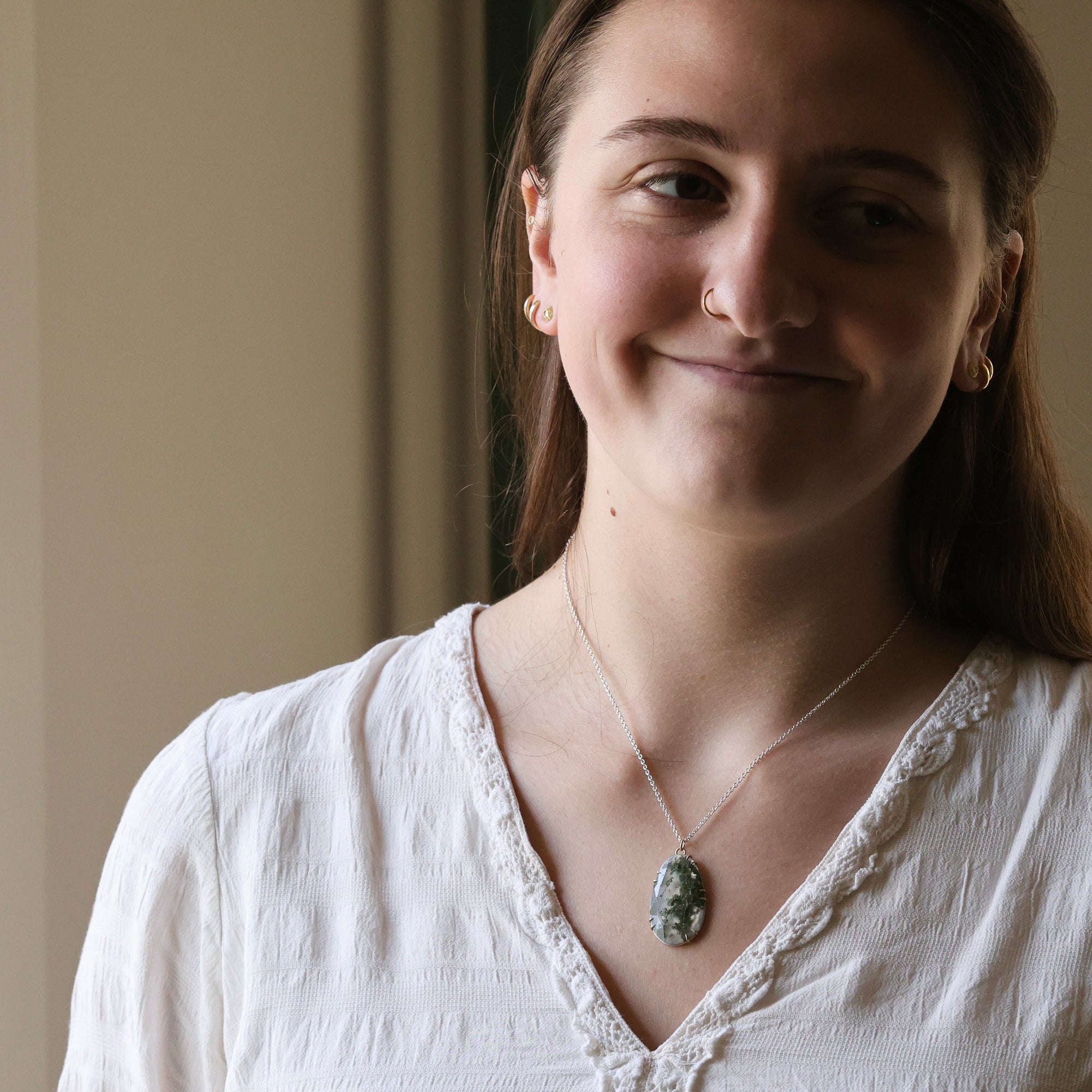 Woman wearing a white blouse with a necklace against a neutral background