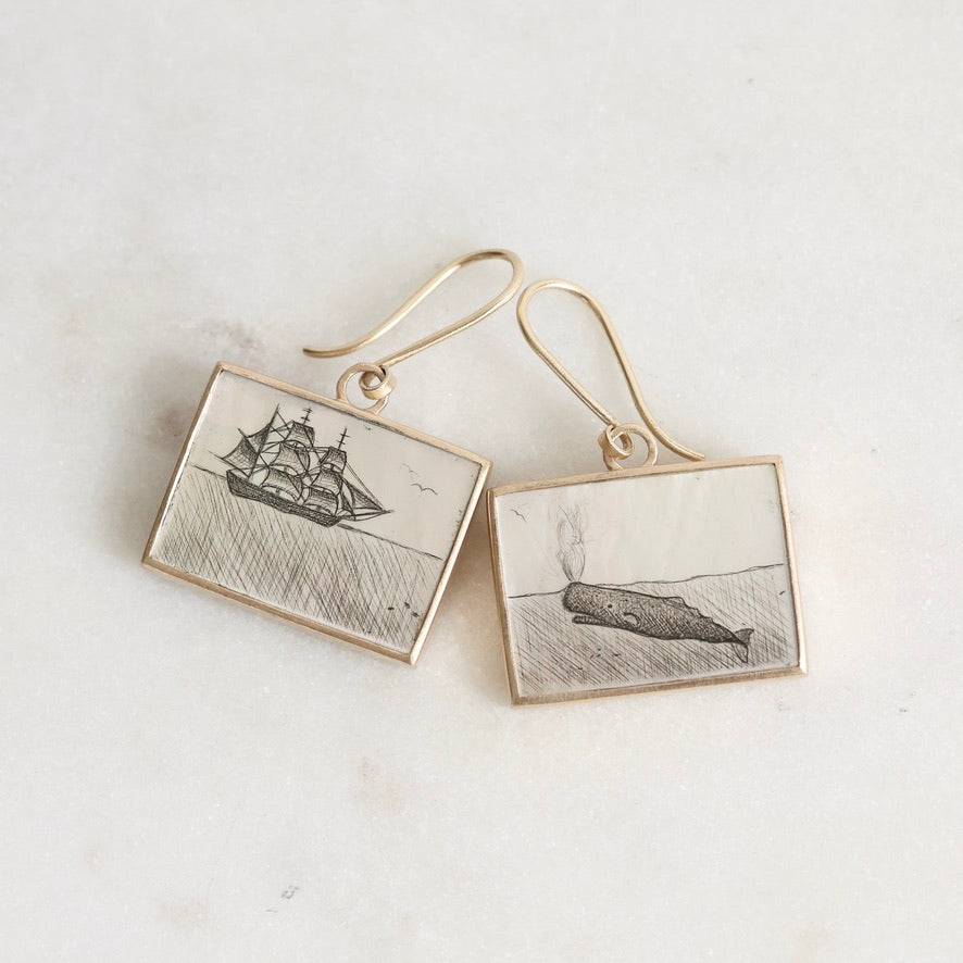 Pair of earrings with ship and whale illustrations on a light background