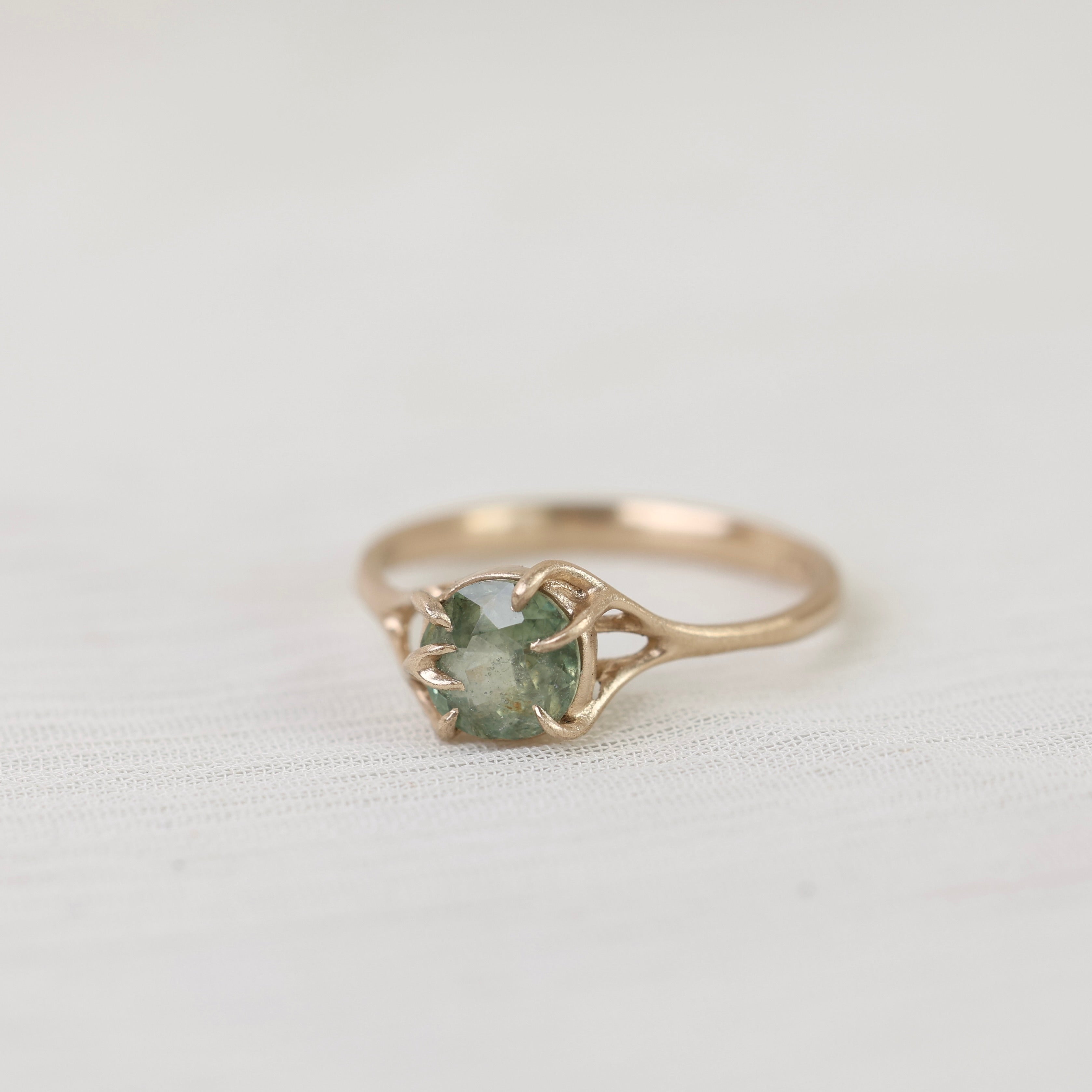 Gold ring with a green gemstone on a light gray background