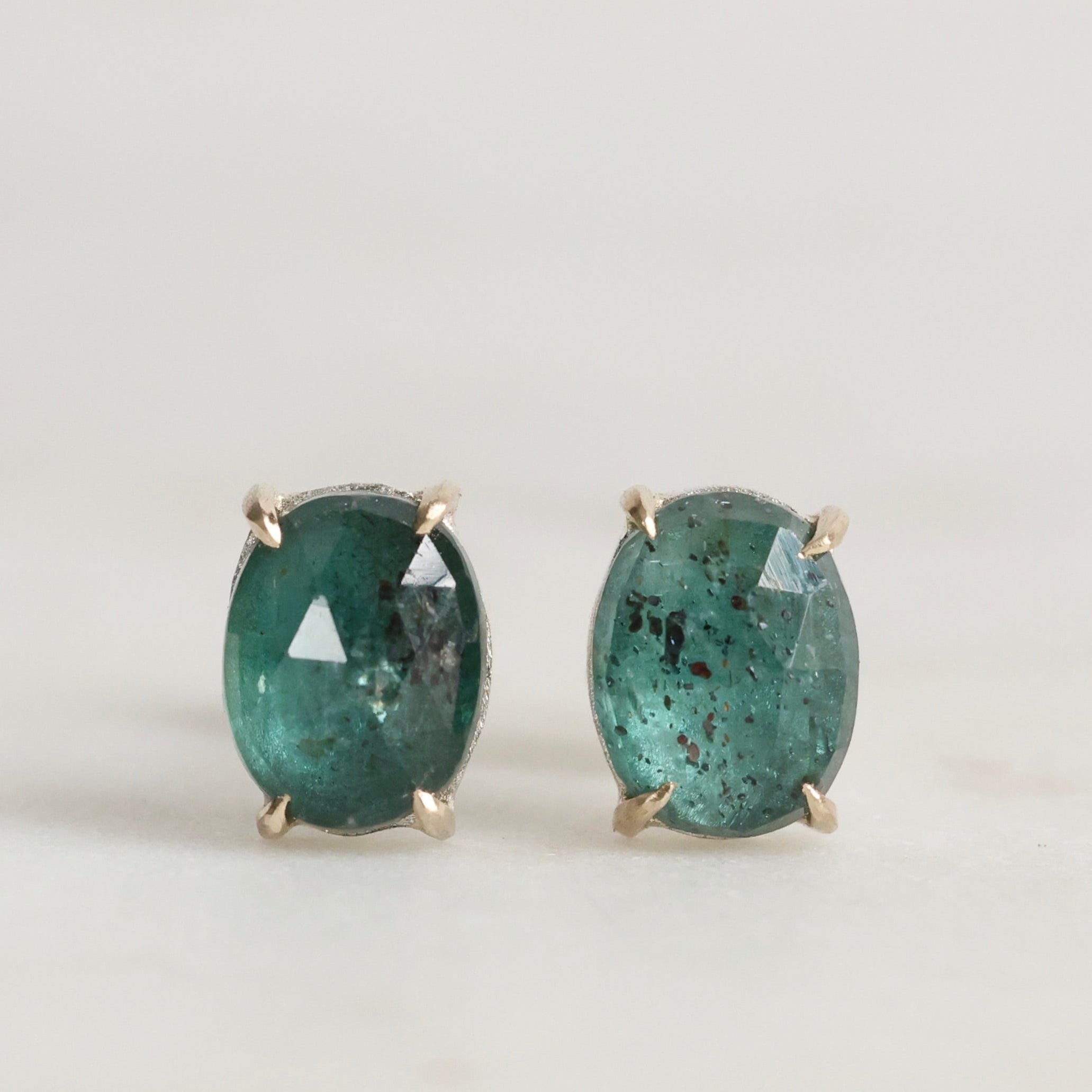 Pair of green gemstone stud earrings on a light gray background