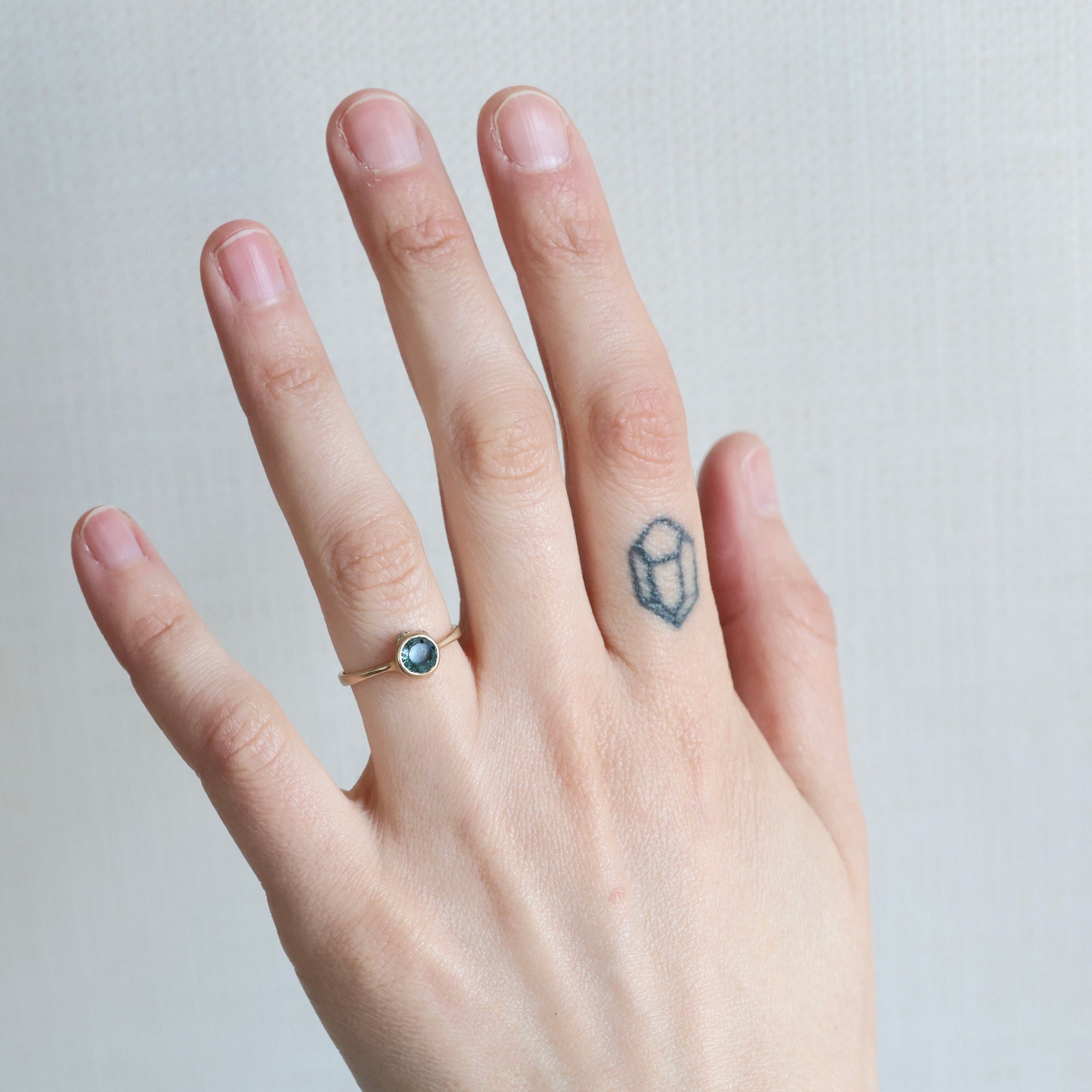 Hand wearing a ring with a small gemstone on a plain background