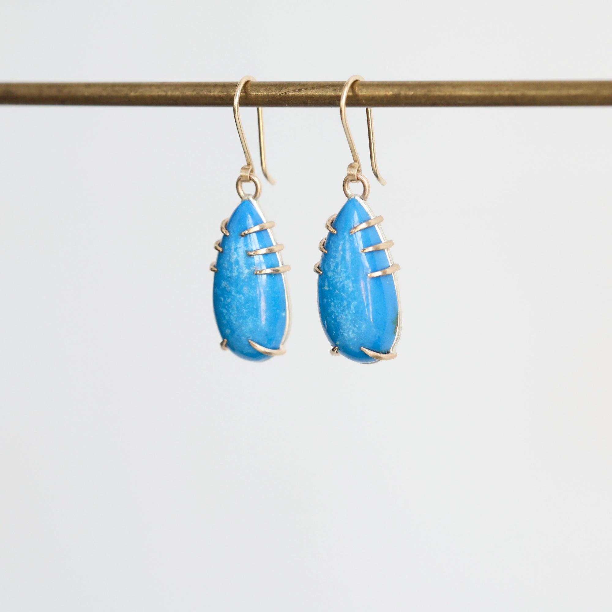Pair of blue teardrop earrings with gold accents on a white background