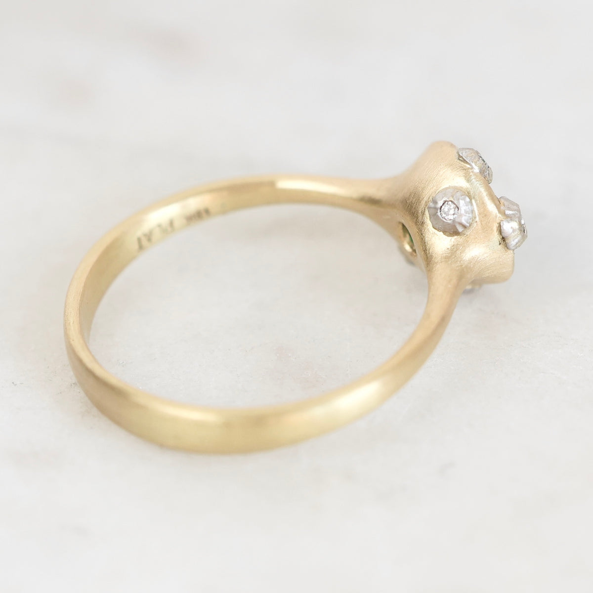 A gold ring with a sculptural, organic-shaped setting featuring three small clear gemstones, photographed on a light marble surface.