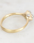 A gold ring with a sculptural, organic-shaped setting featuring three small clear gemstones, photographed on a light marble surface.