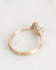 A gold ring with a small cluster of barnacles on a light, off-white marble surface.