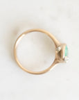 A gold ring with a small green oval gemstone and two accent barnacles, photographed on a light marble-like surface.