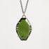 A faceted green gemstone pendant necklace with a dark metal chain and gold-toned prong settings, shown against a light gray background.