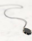A black pendant necklace with a faceted geometric design, held in gold-toned prong settings on a delicate chain, resting on a light marble surface.