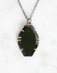 A faceted dark green gemstone pendant necklace with a silver-toned chain and bezel setting, displayed on a white marble background.