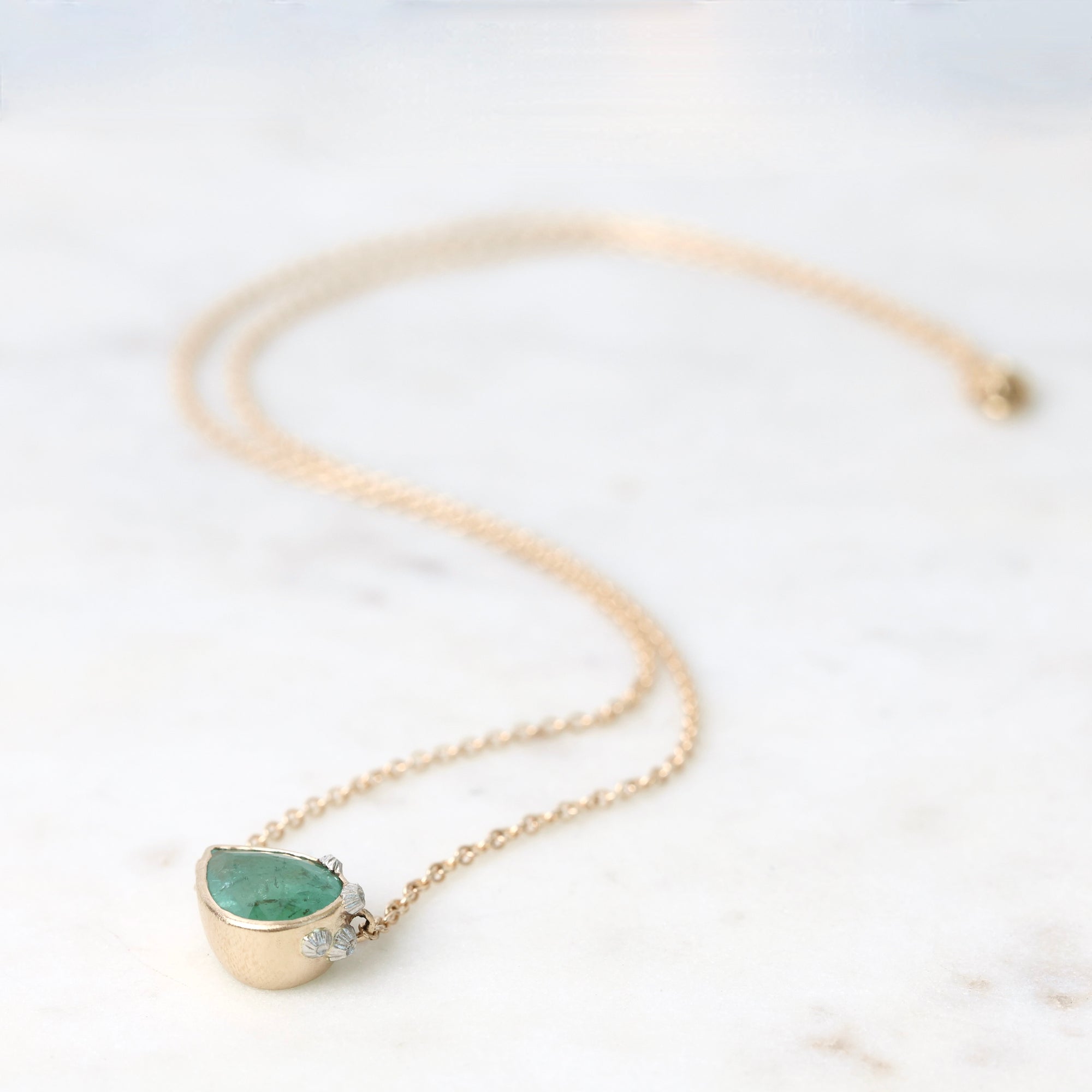 Gold necklace with a green gemstone pendant on a white marble surface