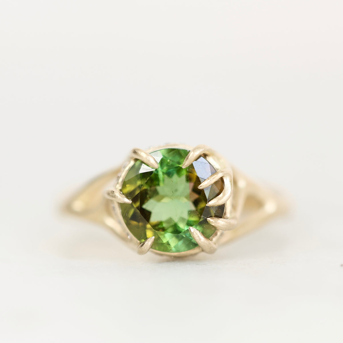 A yellow gold ring featuring a round-cut green gemstone in a prong setting, shown against a plain white background.