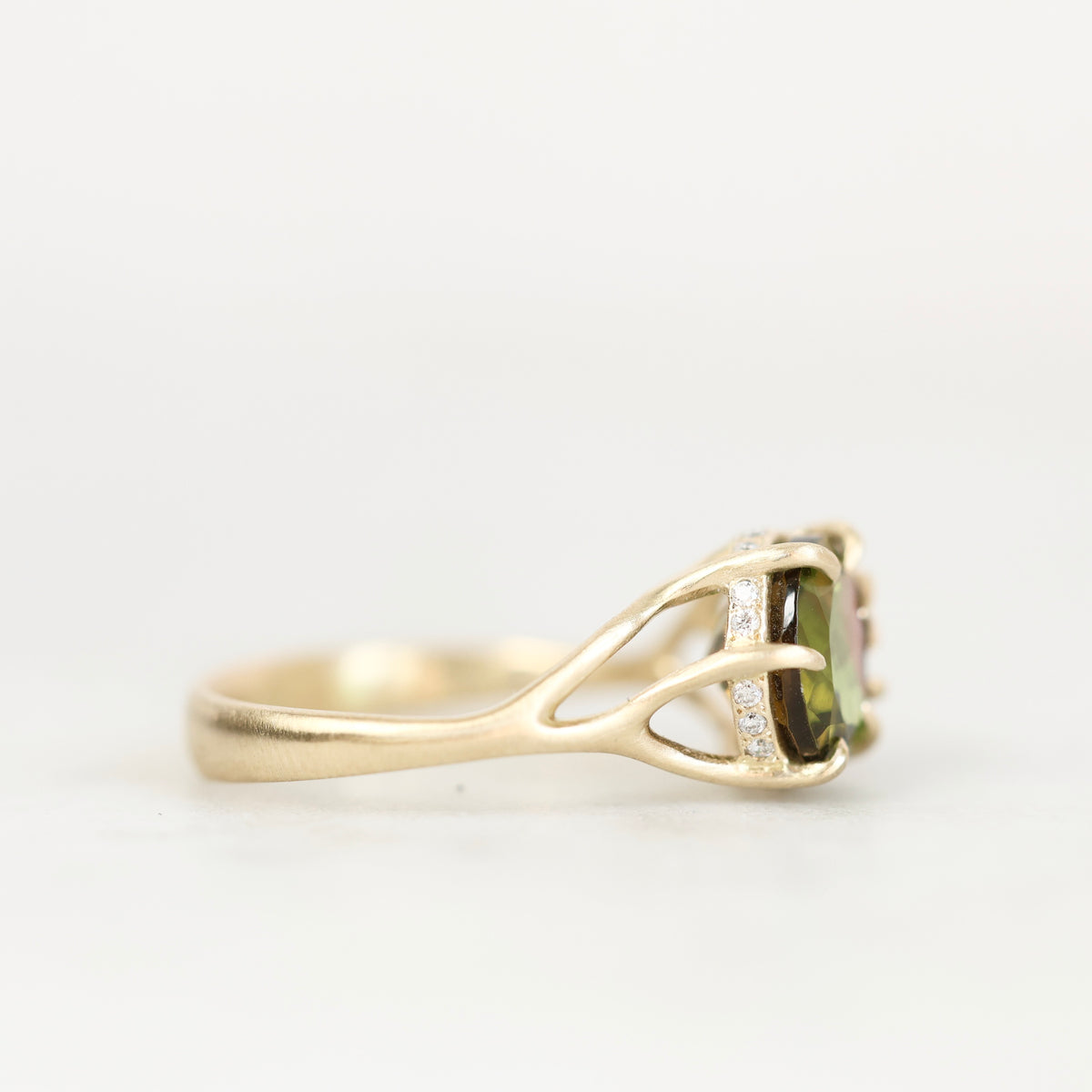 A yellow gold ring featuring a rectangular green gemstone in a prong setting with small clear accent stones, shown against a plain white background.