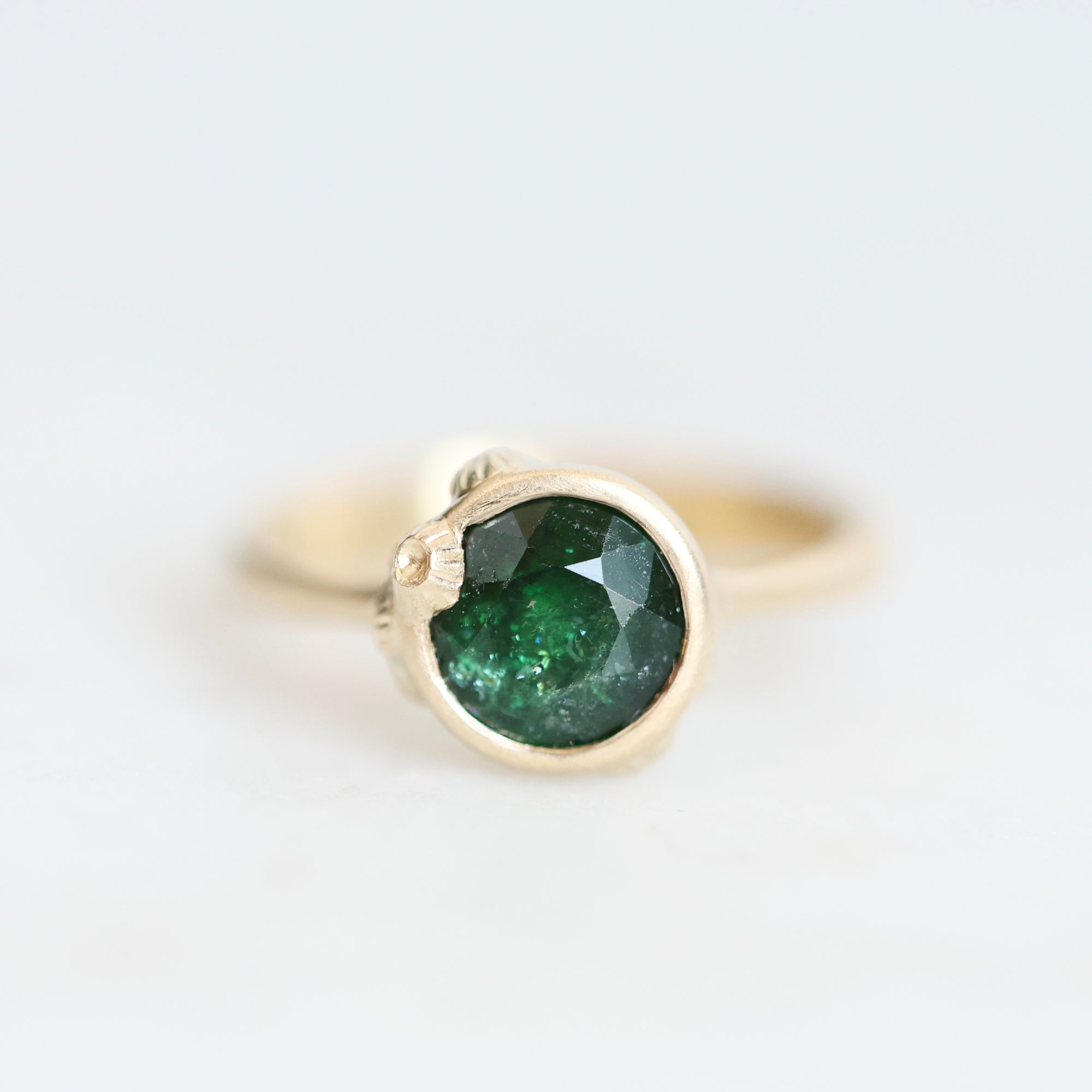 Green gemstone set in gold bezel with barnacle details