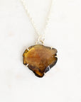 A silver necklace featuring a raw, irregularly shaped amber-brown gemstone pendant, displayed on a clean white background.