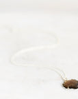 A delicate silver chain necklace with a small, irregular-shaped brown gemstone pendant, resting on a light marble surface.