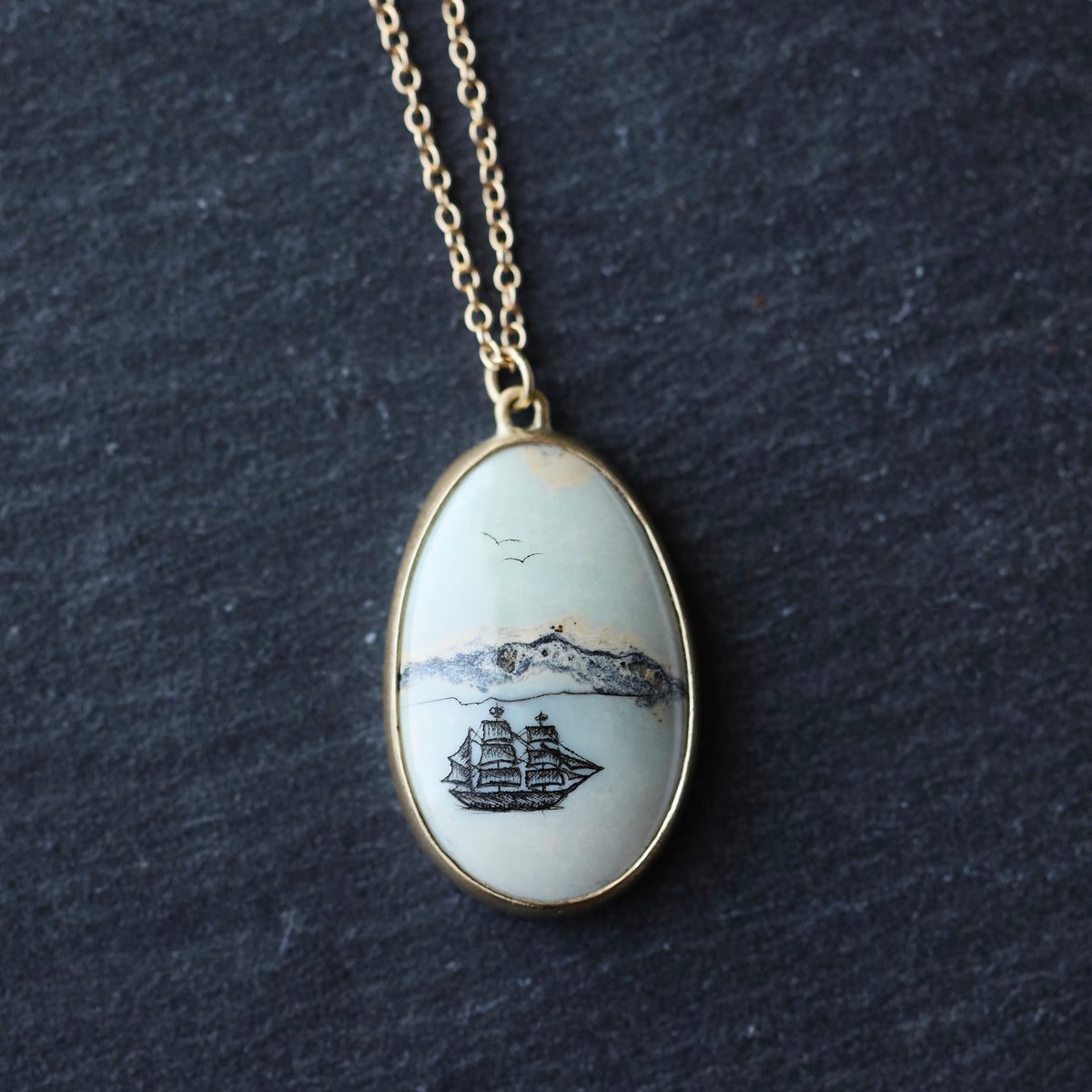 Close up of a necklace featuring a white stone with a ship engraving 