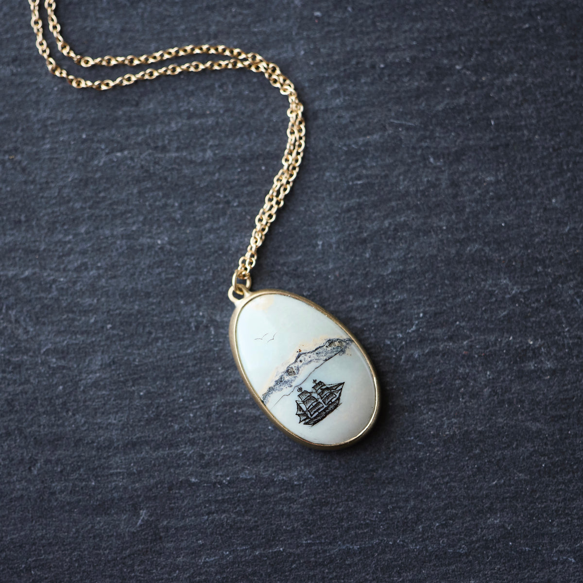 Necklace on a gold chain featuring a white stone with a ship engraving 