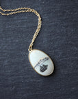 Necklace on a gold chain featuring a white stone with a ship engraving 