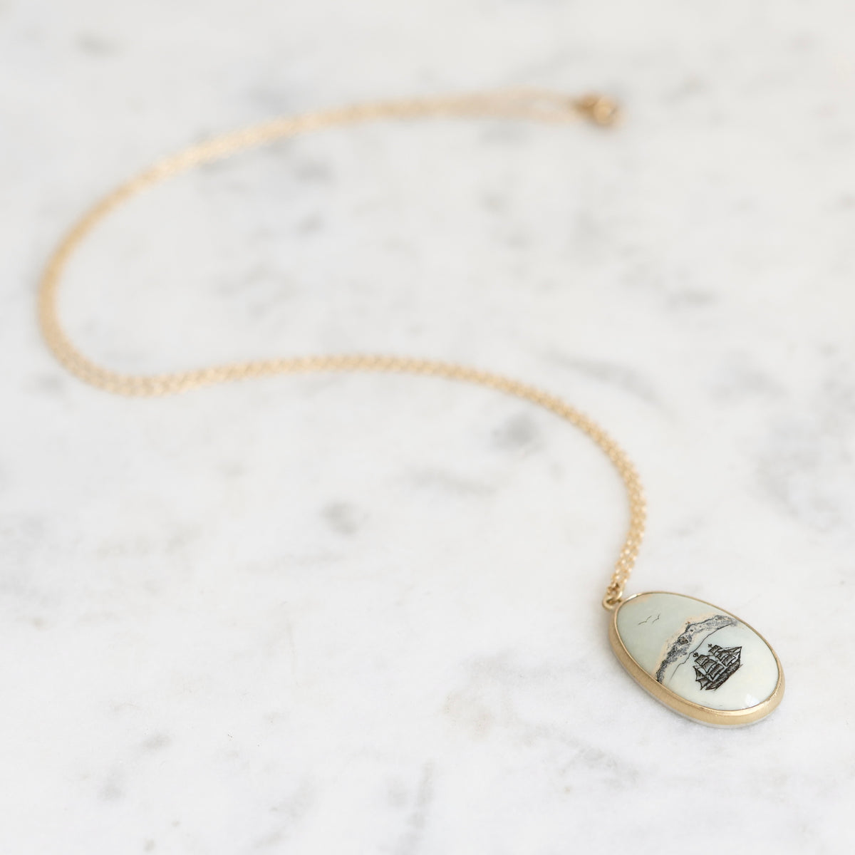 Necklace with a gold chain laid out. The pendant is a white stone with a ship engraving on it. 